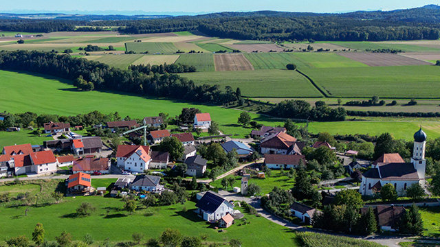 Ein Blick von oben zeigt den kleinen Ort Neuburg mit einer Kirche, Häusern, Wäldern und grünen Feldern.